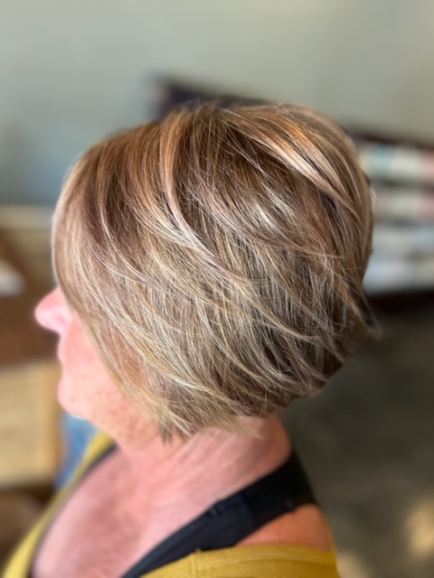 Side profile of a person with a short layered blonde haircut featuring light brown and platinum highlights, indoors.